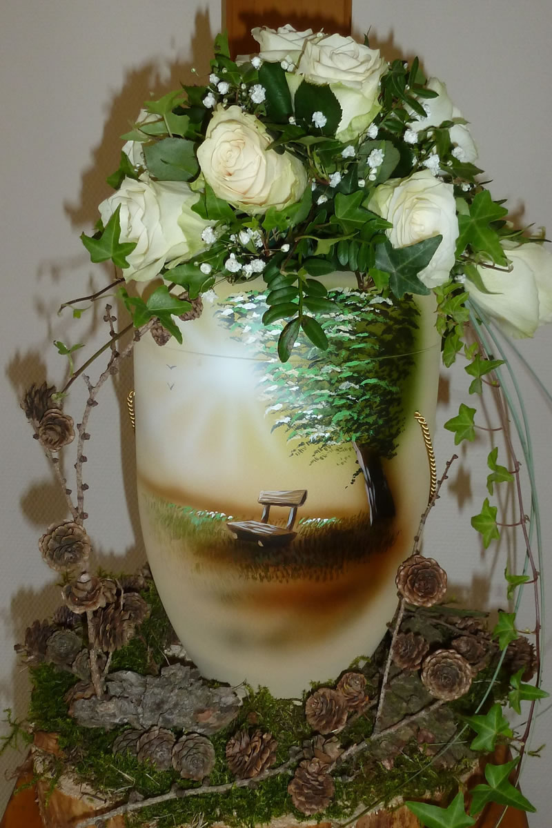 Eine weiß und braun gehaltene Urne mit einer Bank vor einem Baum im Sonnenschein Eine weiß und braun gehaltene Urne mit einer Bank vor einem Baum im Sonnenschein