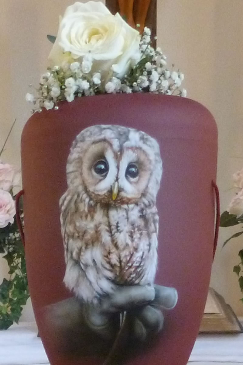 Eine rotbraune Urne mit einem Uhu sitzend auf einer Hand Eine rotbraune Urne mit einem Uhu sitzend auf einer Hand