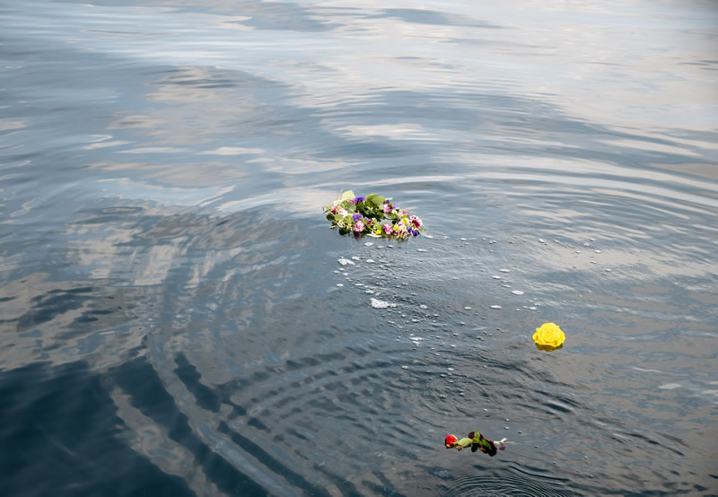 Ein Blumenkranzu sowie eine einzelne gelbe und rote Rose schwimmen auf der Wasseroberfläche Ein Blumenkranzu sowie eine einzelne gelbe und rote Rose schwimmen auf der Wasseroberfläche